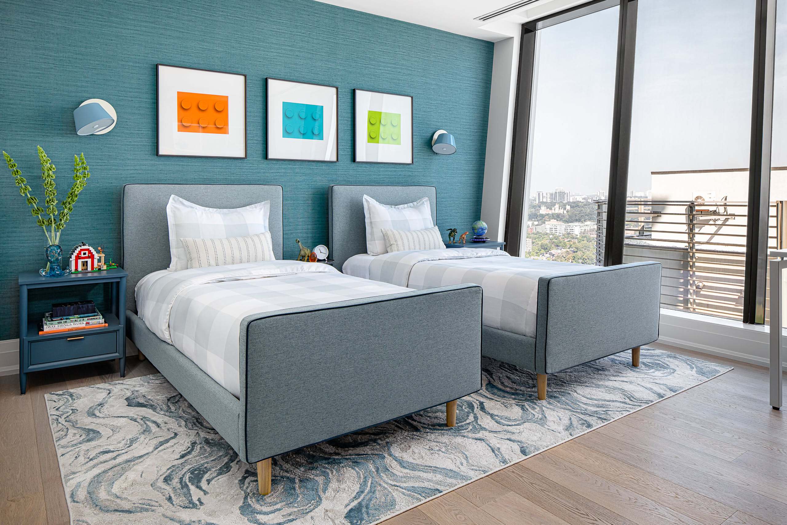 Monochromatic blue boys' bedroom in Yorkville featuring twin beds, dinosaur decor, and floor-to-ceiling windows with city views.