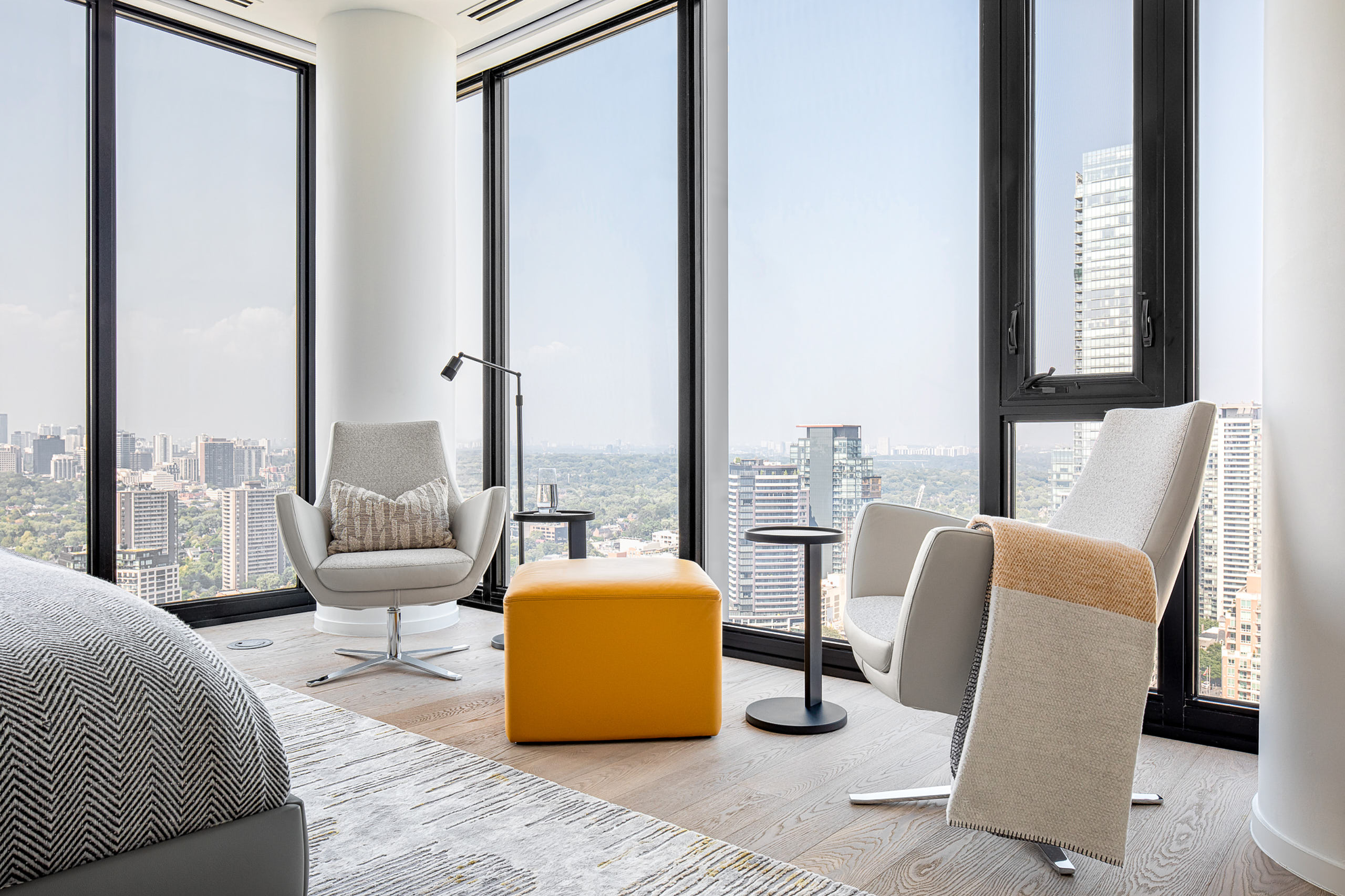 Two Italian swivel armchairs and a mustard ottoman facing panoramic city windows