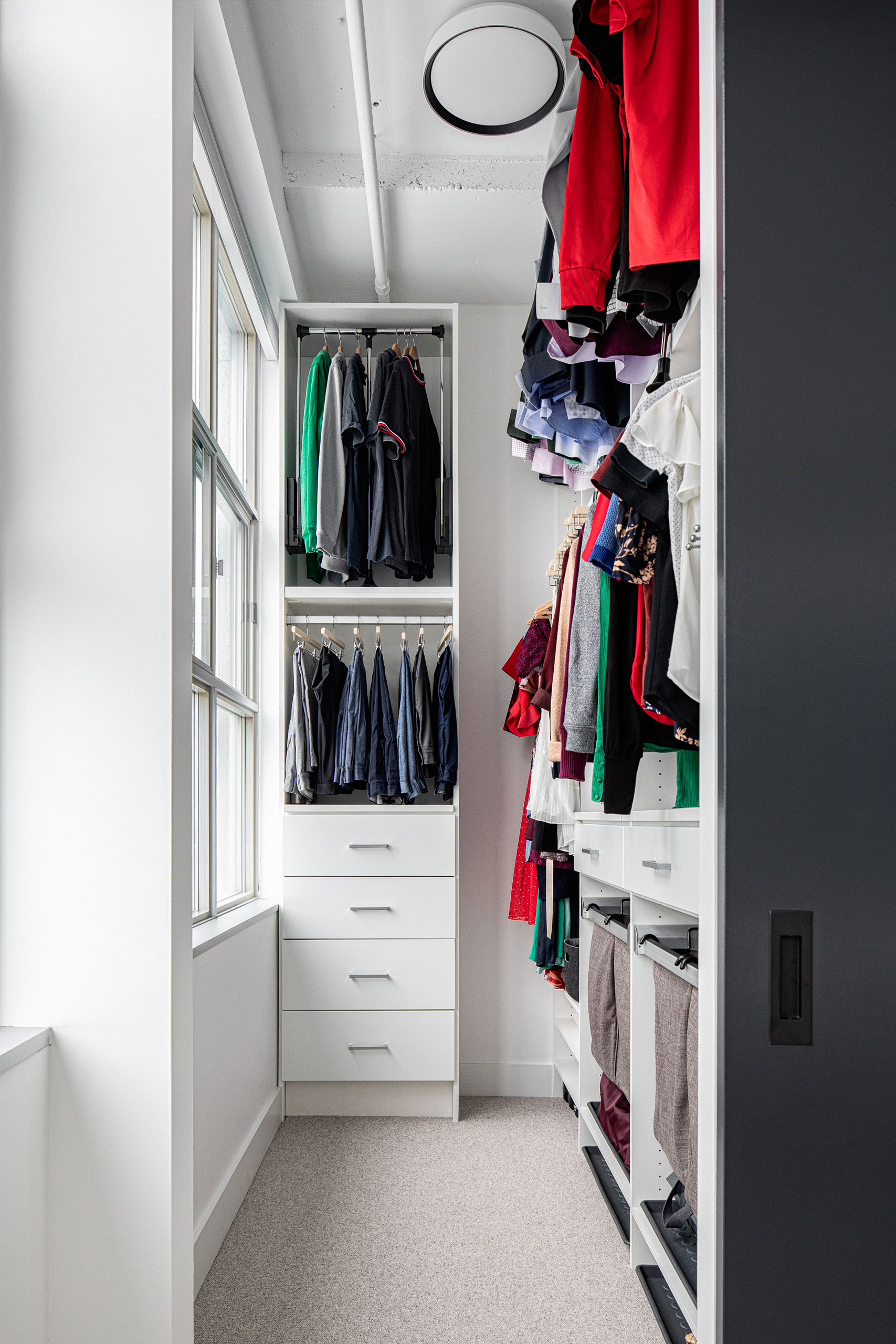 Custom white walk-in closet system in an industrial loft featuring hanging rails, drawers, and ample clothing storage.