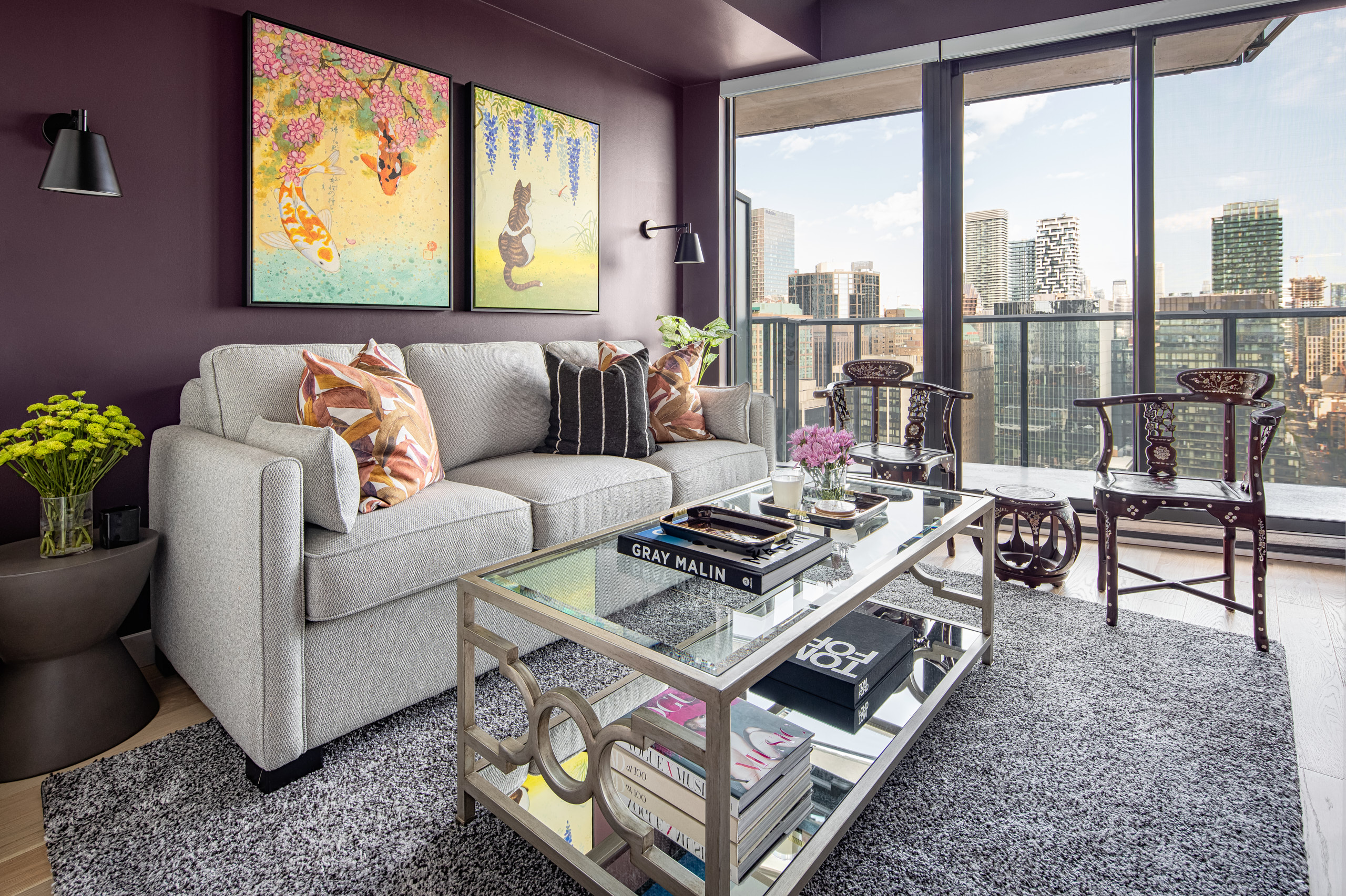 Light grey sofa against a deep purple wall with vibrant artwork and city views