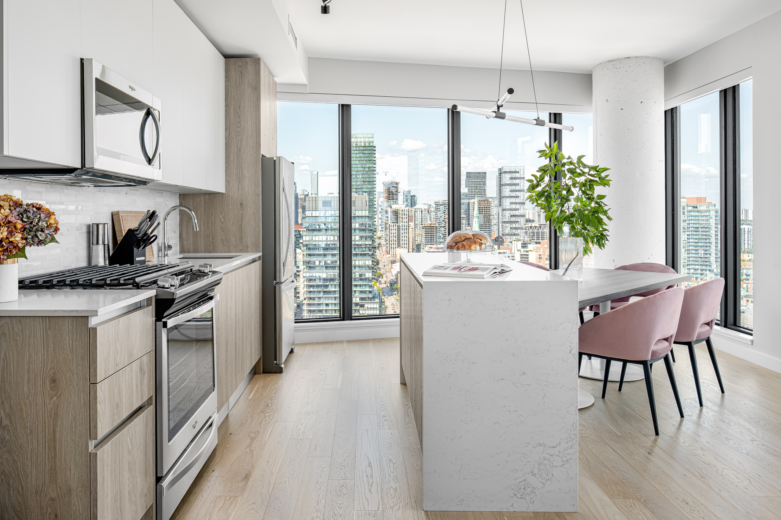 Modern kitchen with white uppers, wood lowers, and a white quartz island with pink chairs