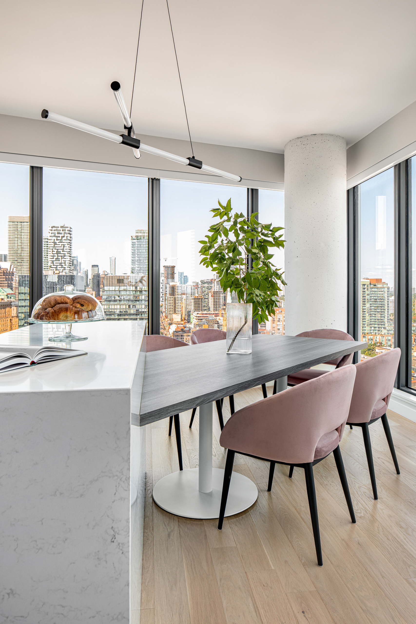 Pink velvet dining chairs around a custom table with a modern linear chandelier and city views