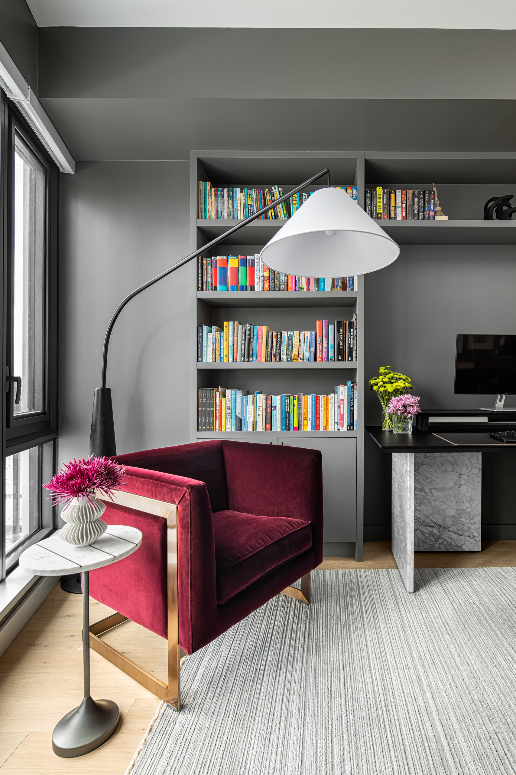 Burgundy velvet armchair with gold base next to a modern floor lamp and grey bookshelves