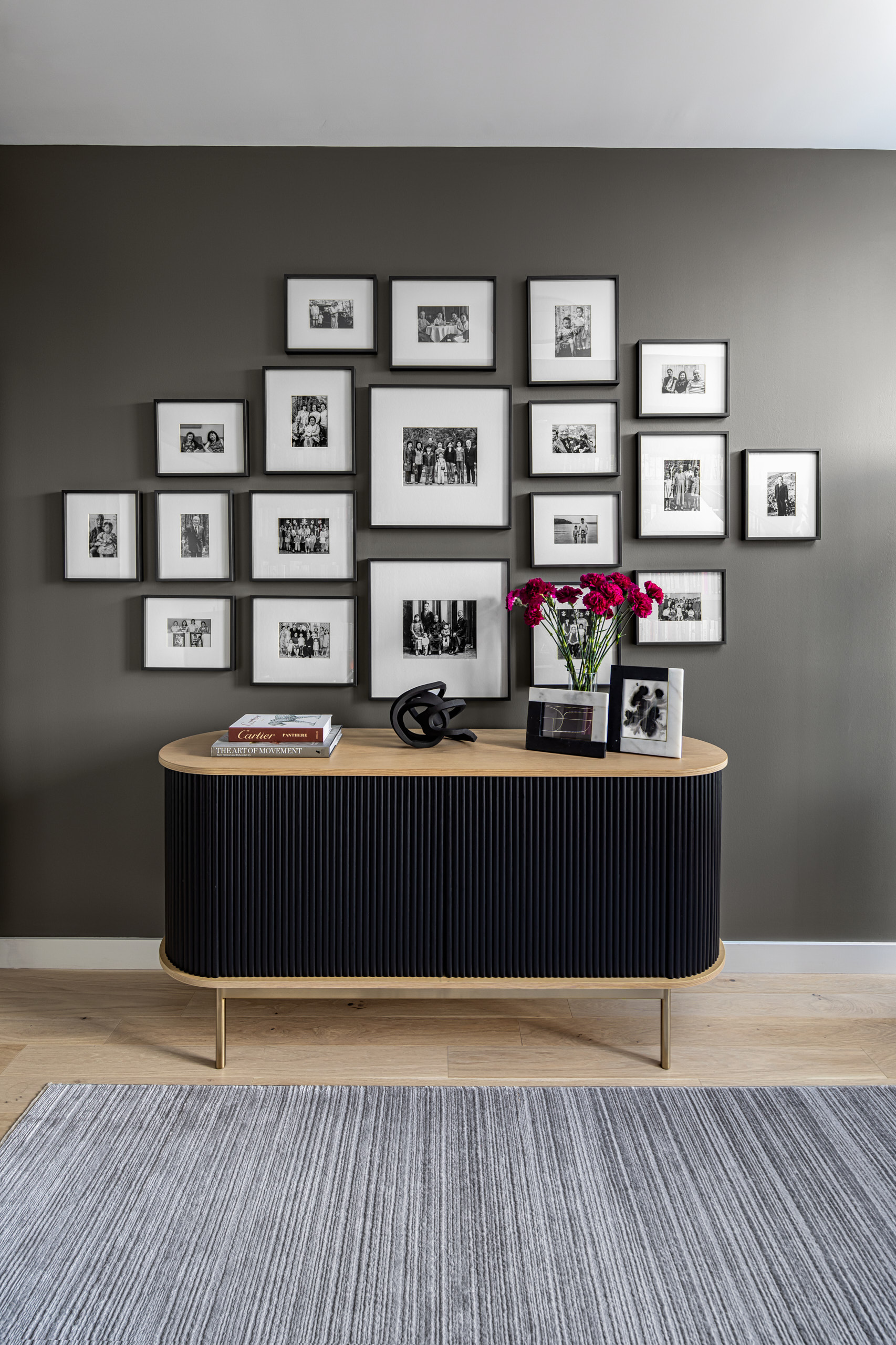 Black fluted sideboard beneath a symmetrical gallery wall of black and white photos on a grey wall