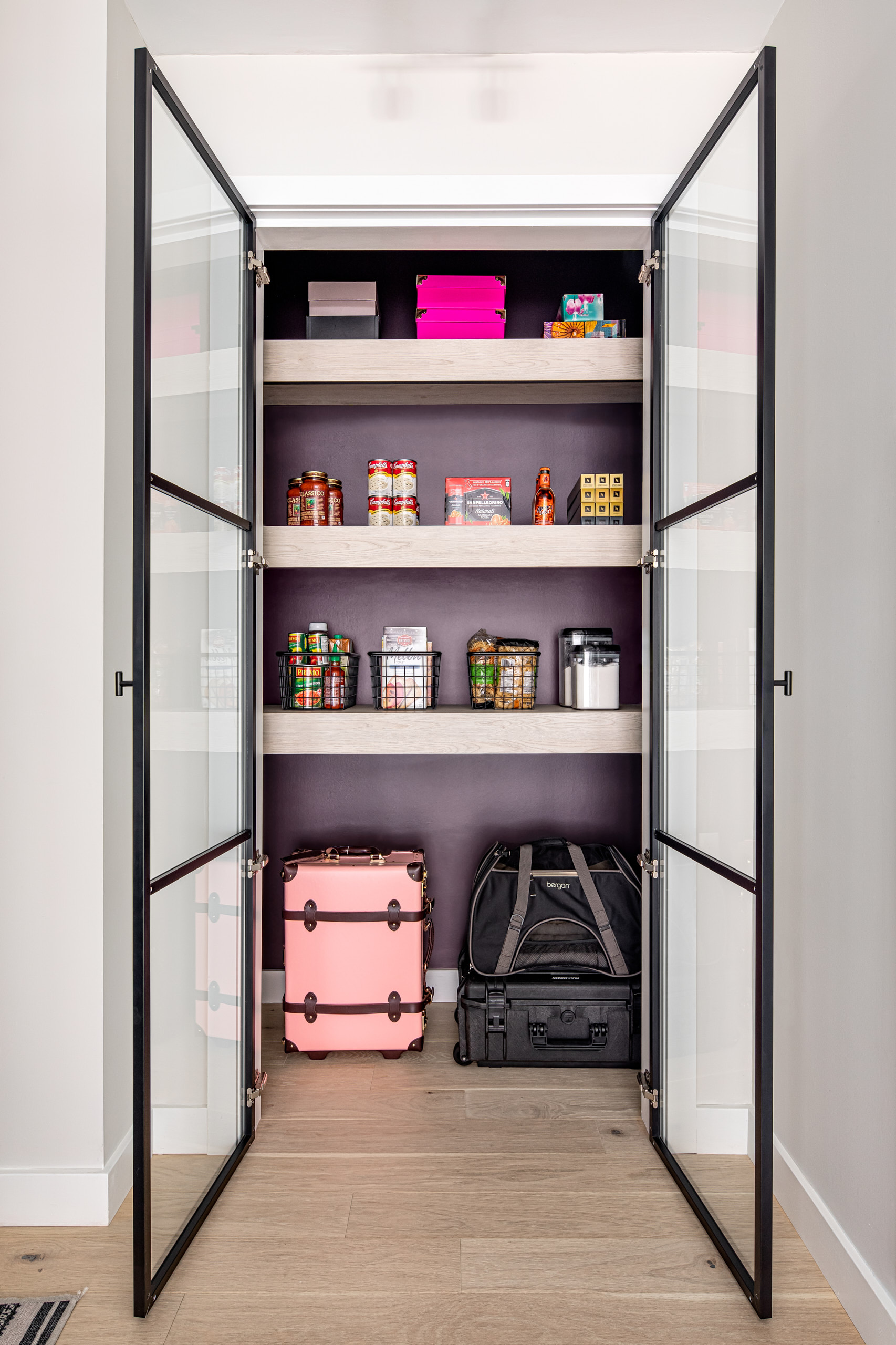 Walk in pantry with black metal glass doors, light wood shelves, and a dark purple back wall