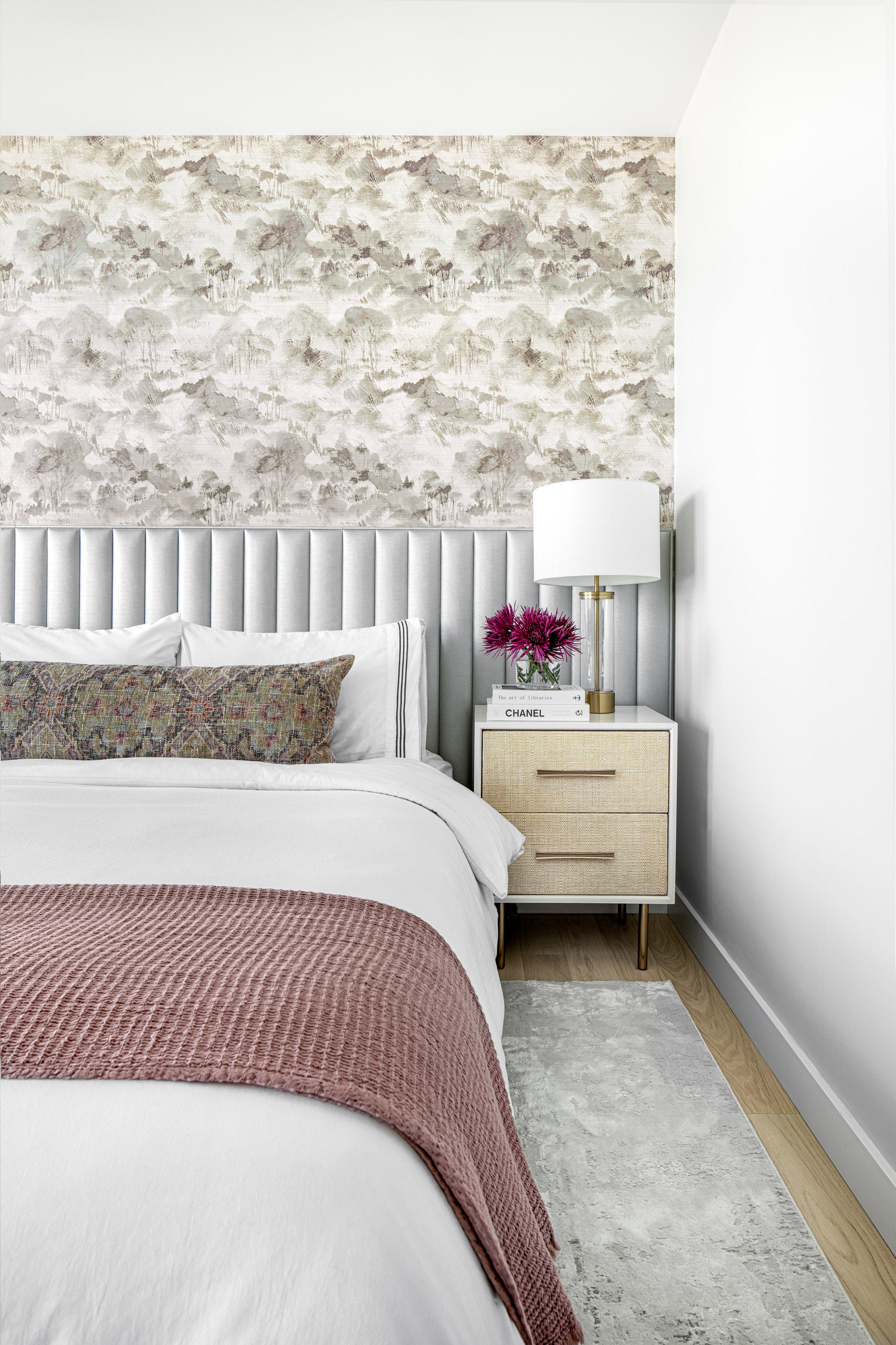 Bedroom with a grey fluted headboard, landscape wallpaper, and a woven nightstand