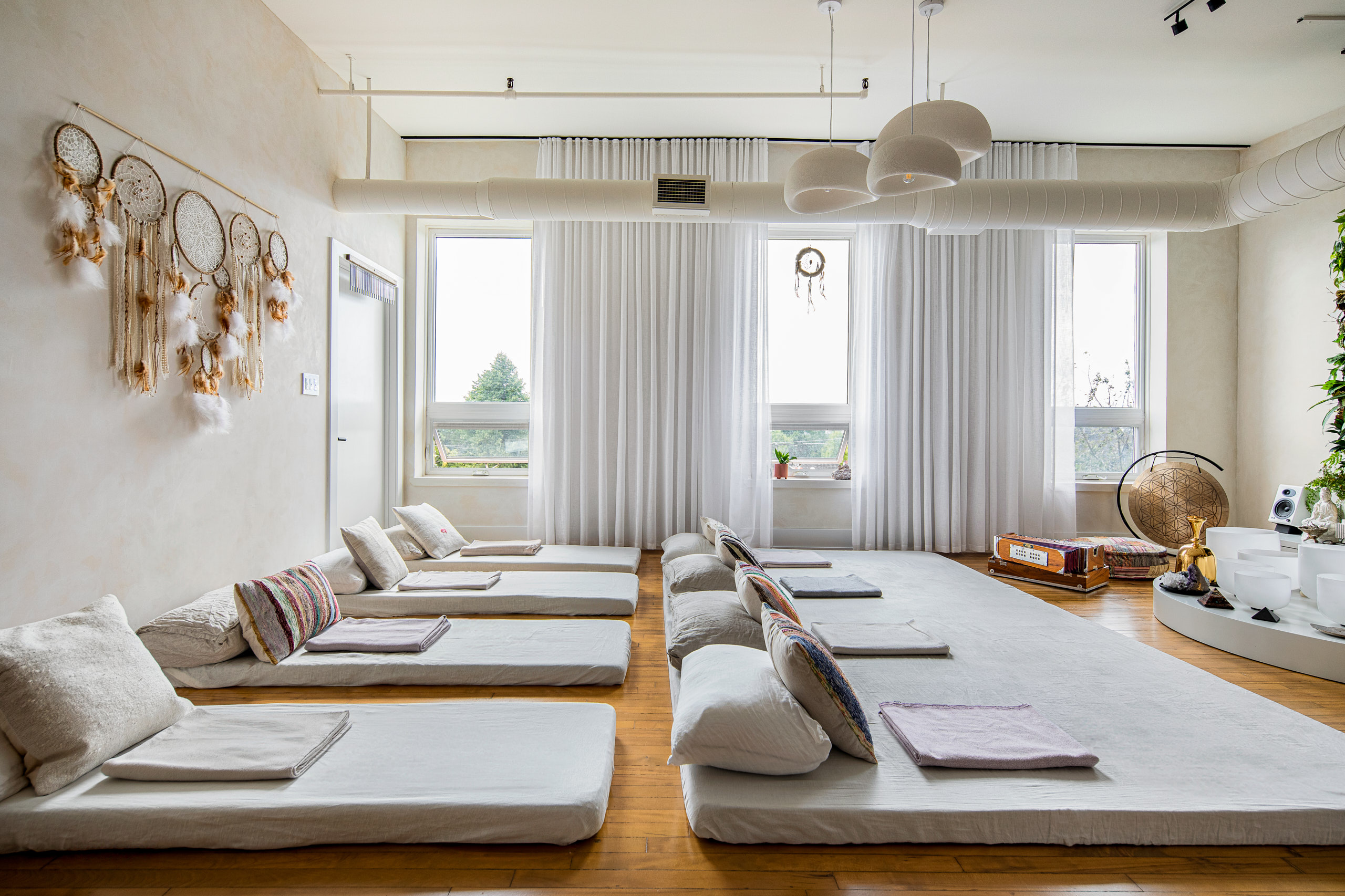 Minimalist wellness studio design highlighting light wood floors, floor-to-ceiling sheers, and a collection of dreamcatchers on limewash walls.