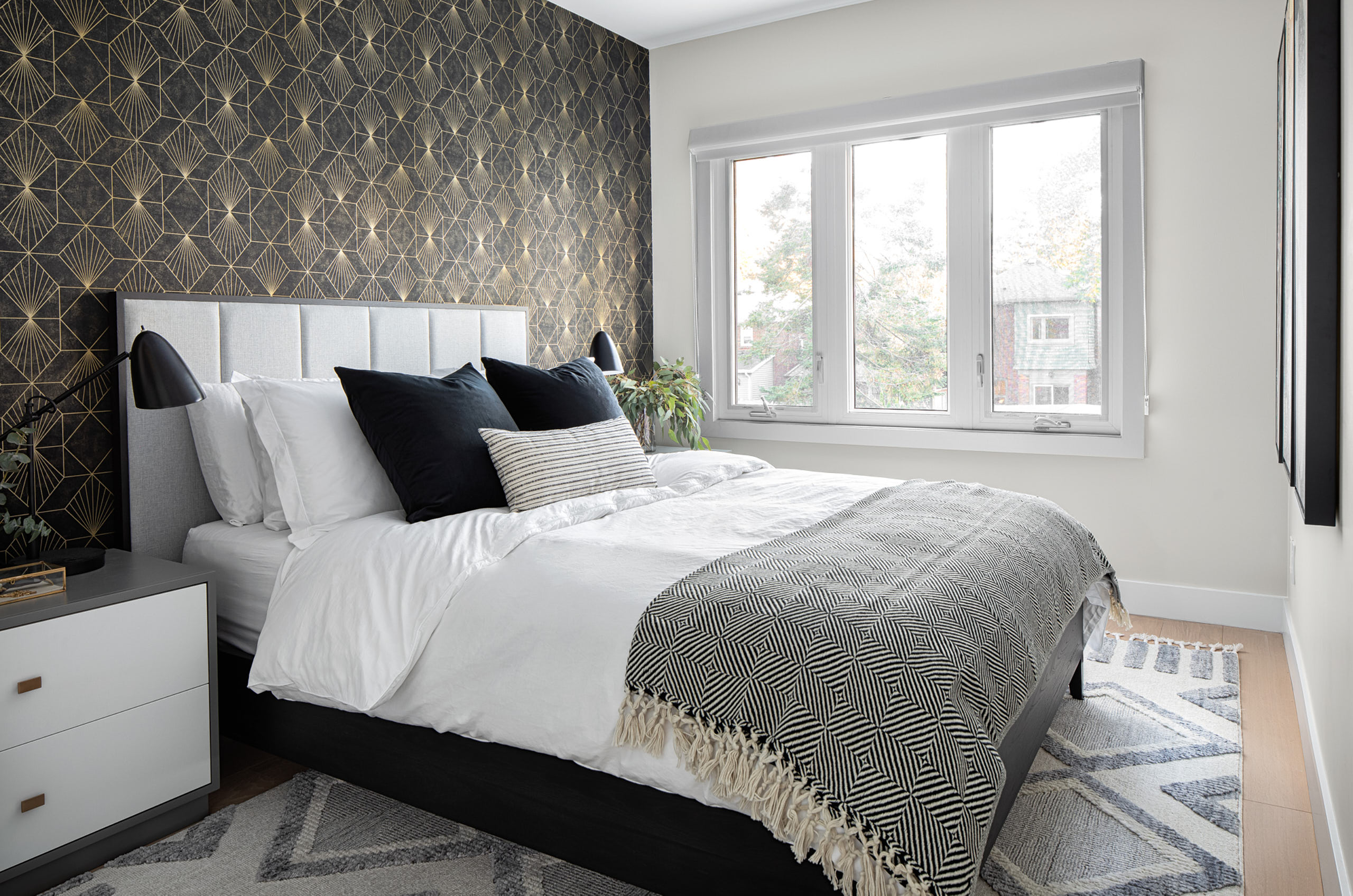 Bedroom with black and gold geometric wallpaper, grey headboard, and patterned blanket