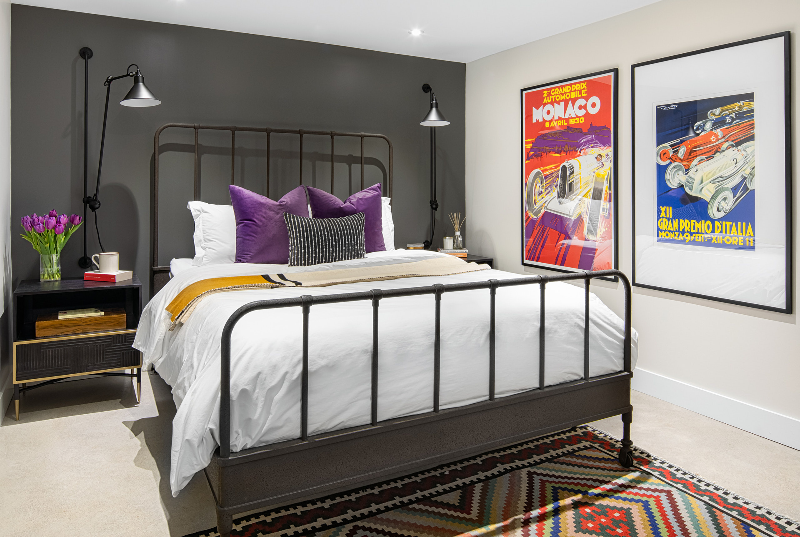 Industrial metal bed with white bedding, purple pillows, and vintage auto racing posters