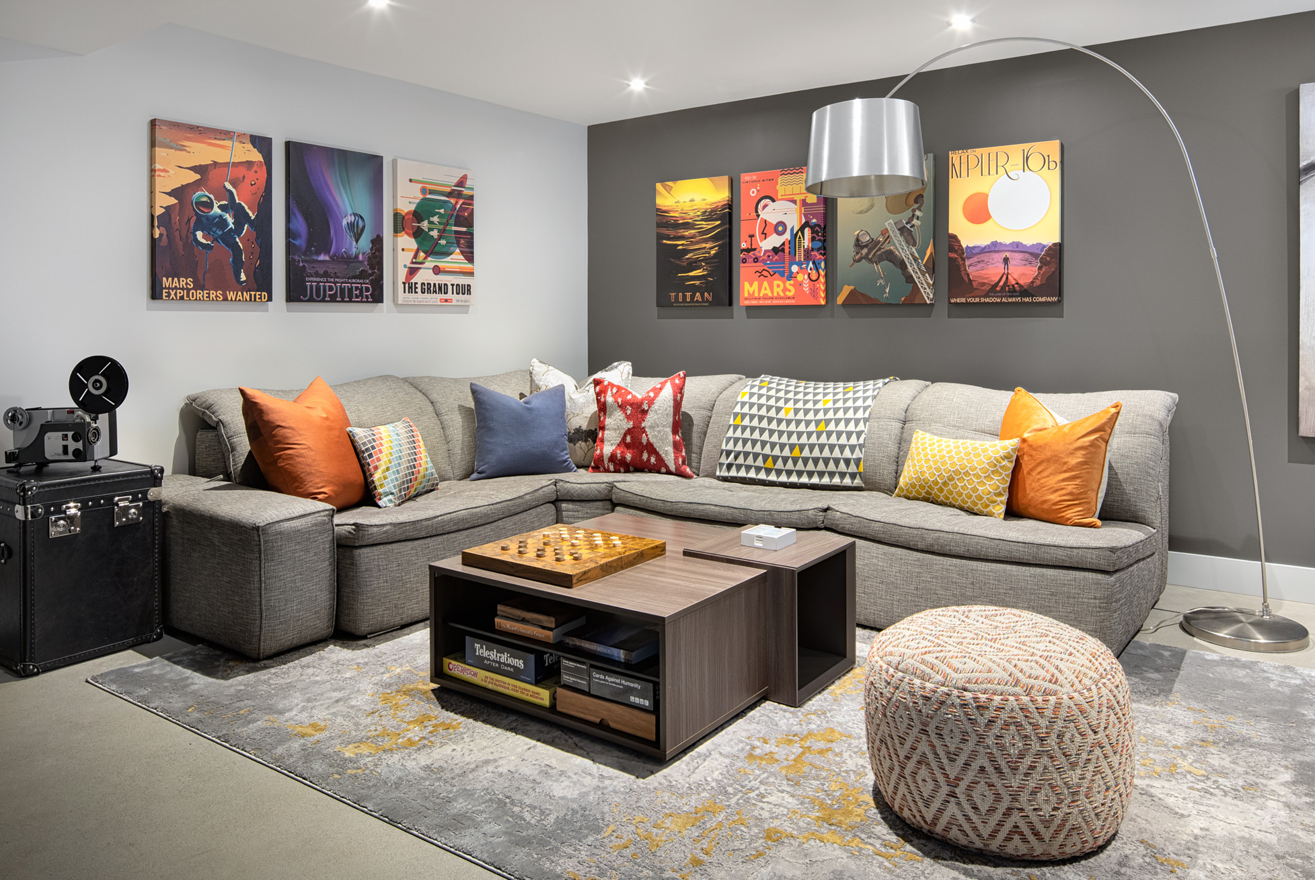 Grey sectional sofa, arched silver floor lamp, and retro space posters in a living area