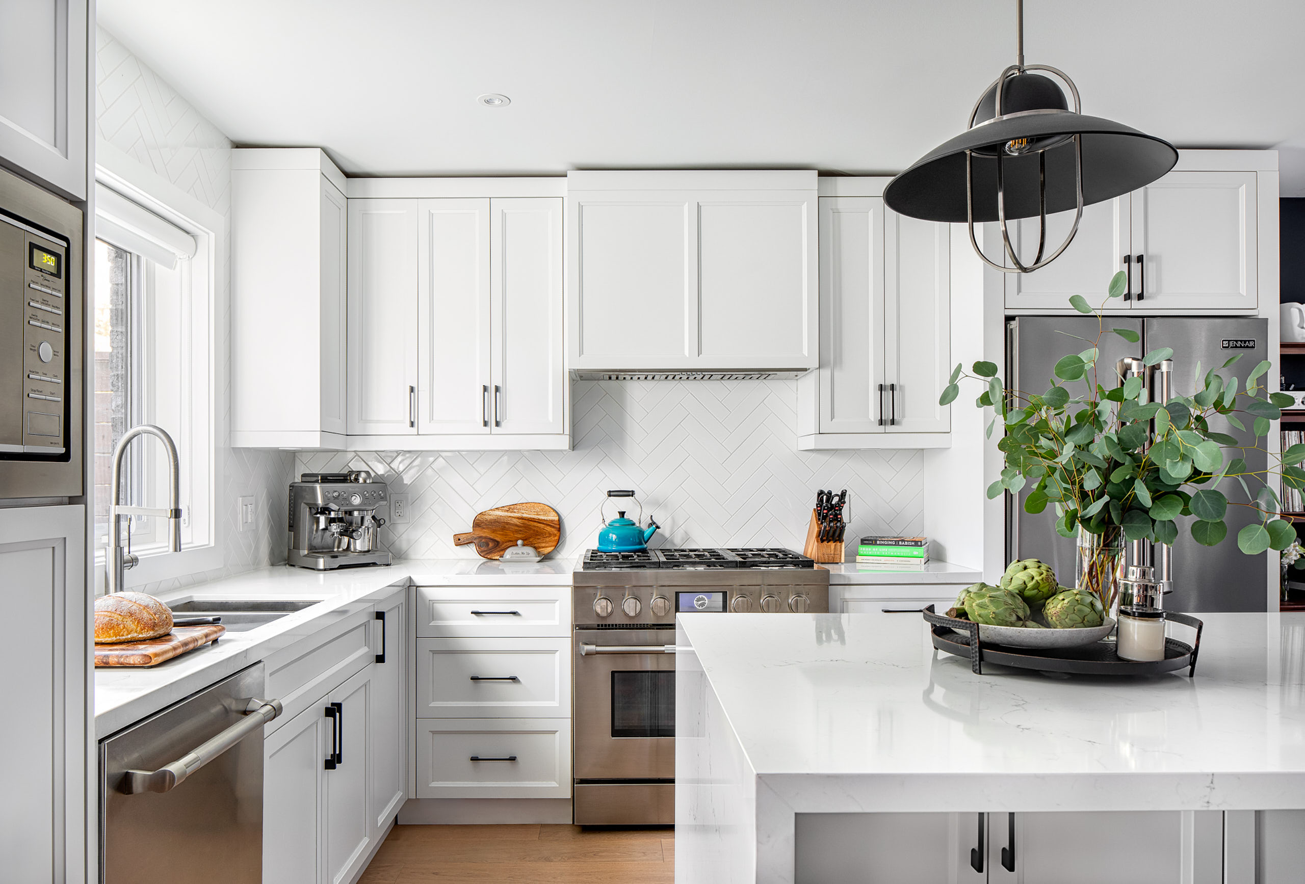 White shaker kitchen cabinets with a white herringbone subway tile backsplash and quartz island