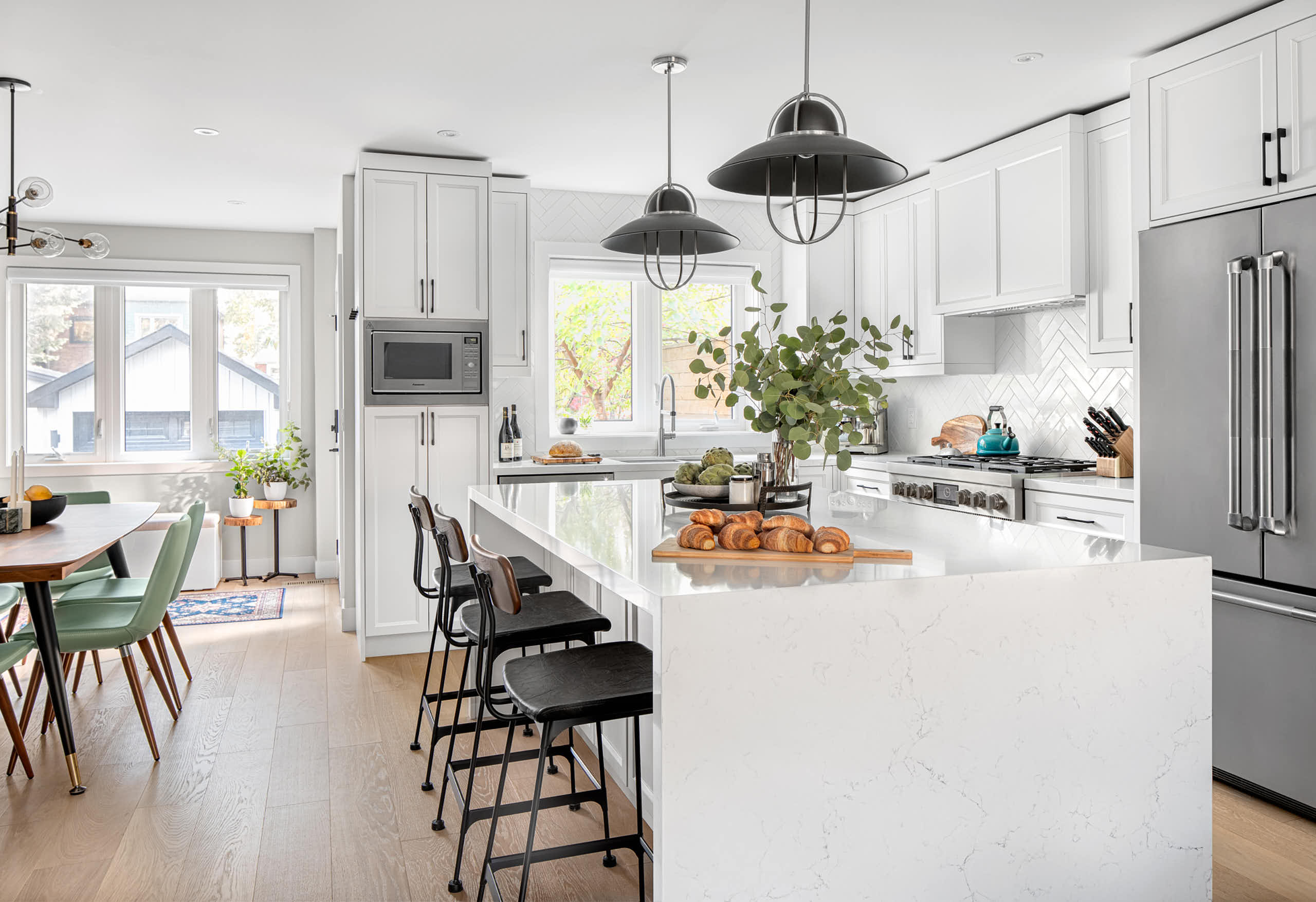 Large white quartz kitchen island with black bar stools and industrial pendant lights