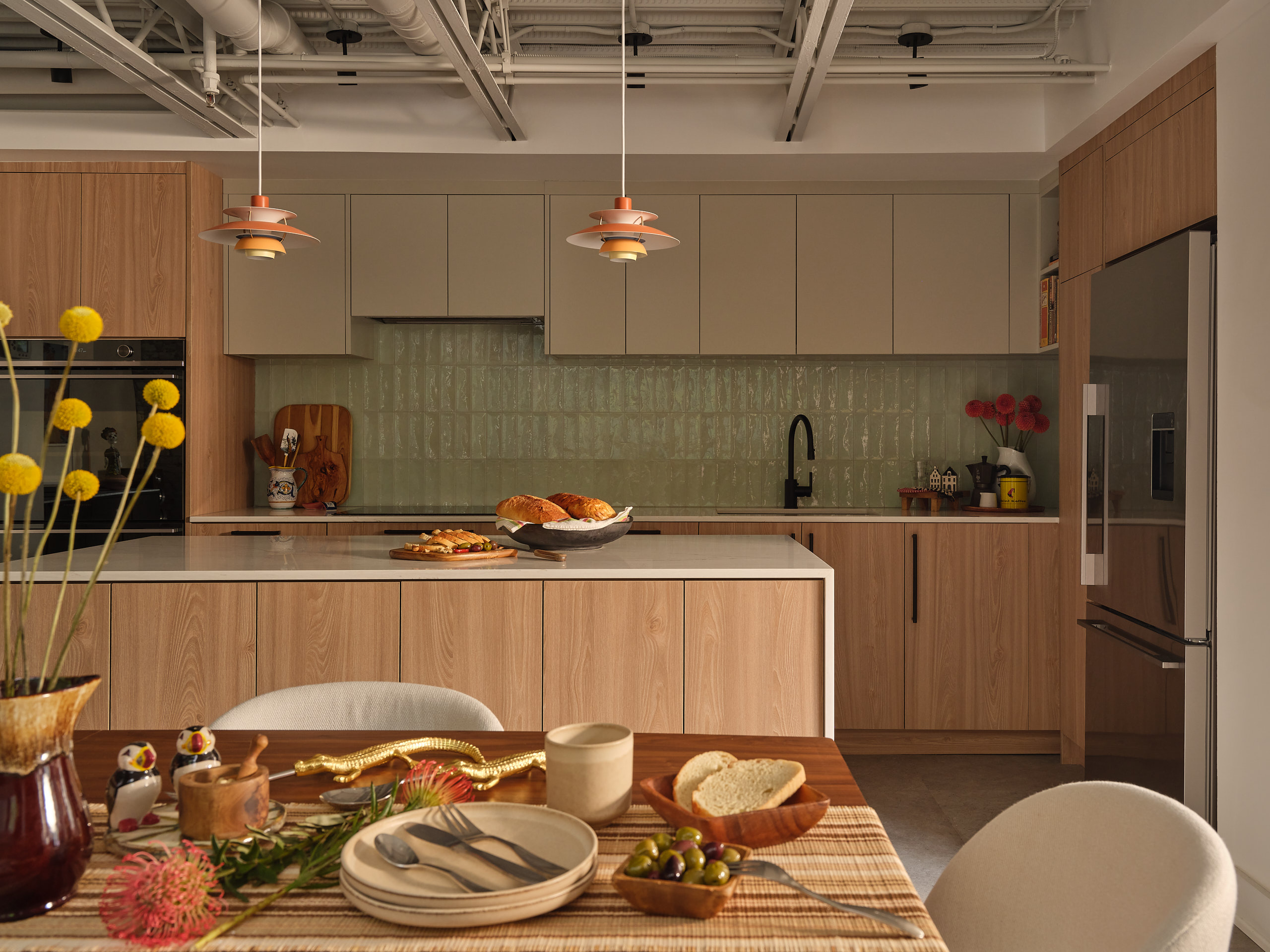 Loft kitchen with sage green tile backsplash, oak cabinetry, and orange pendant lights in Toronto.