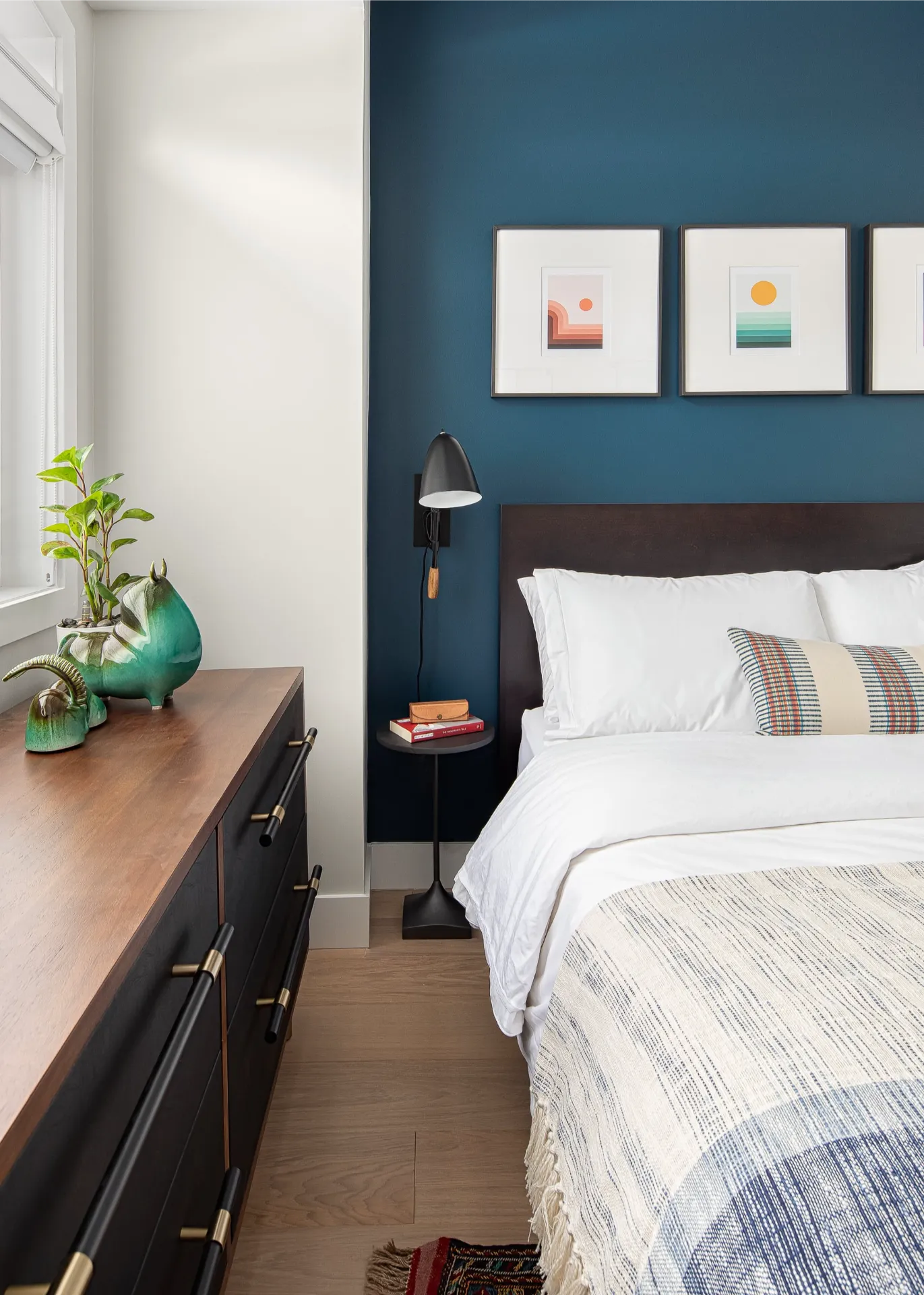 Bed with white linens against a dark blue wall with three framed landscape prints