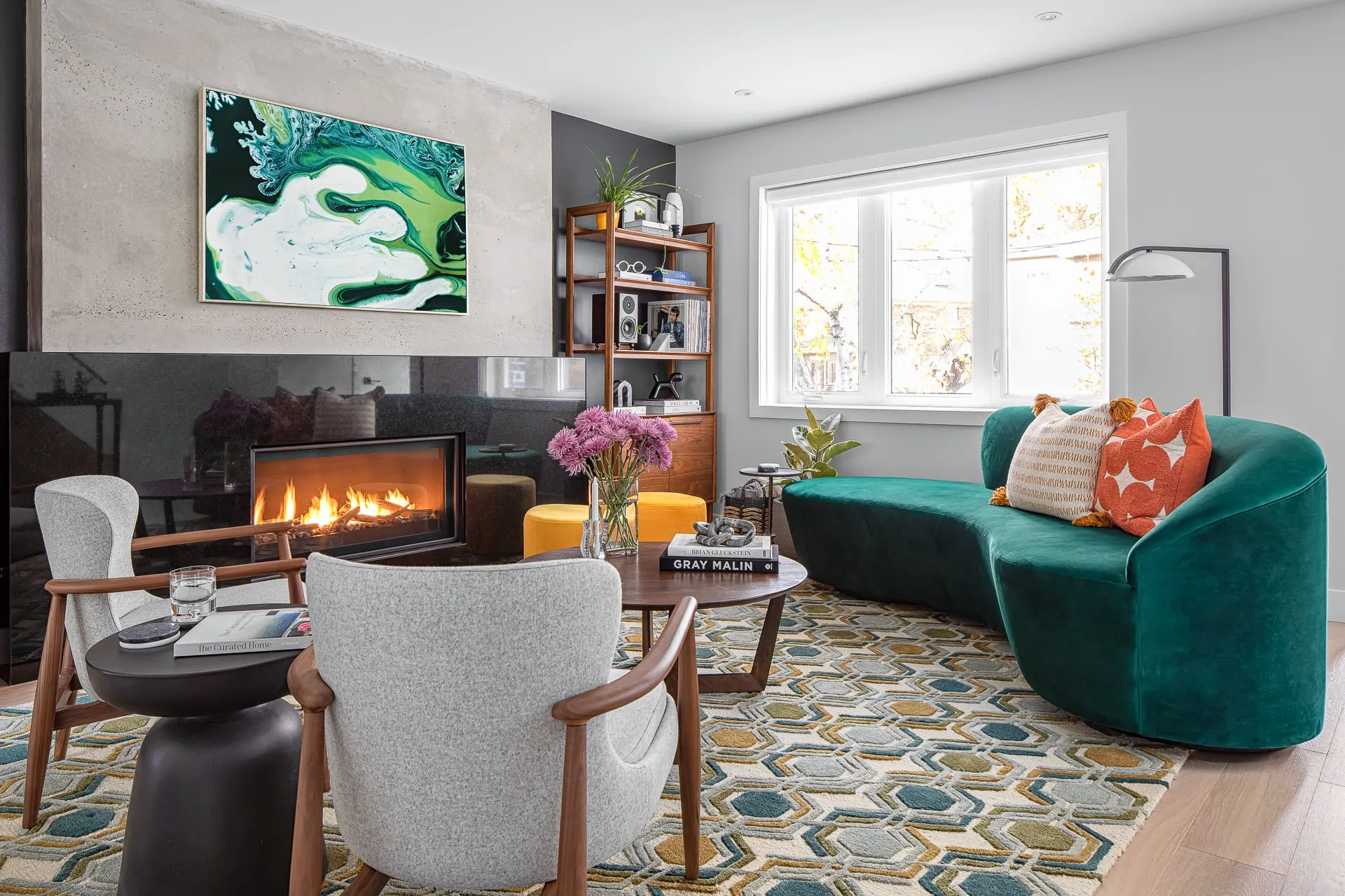 Colourful living room with a green velvet sofa, yellow ottomans, and a concrete fireplace