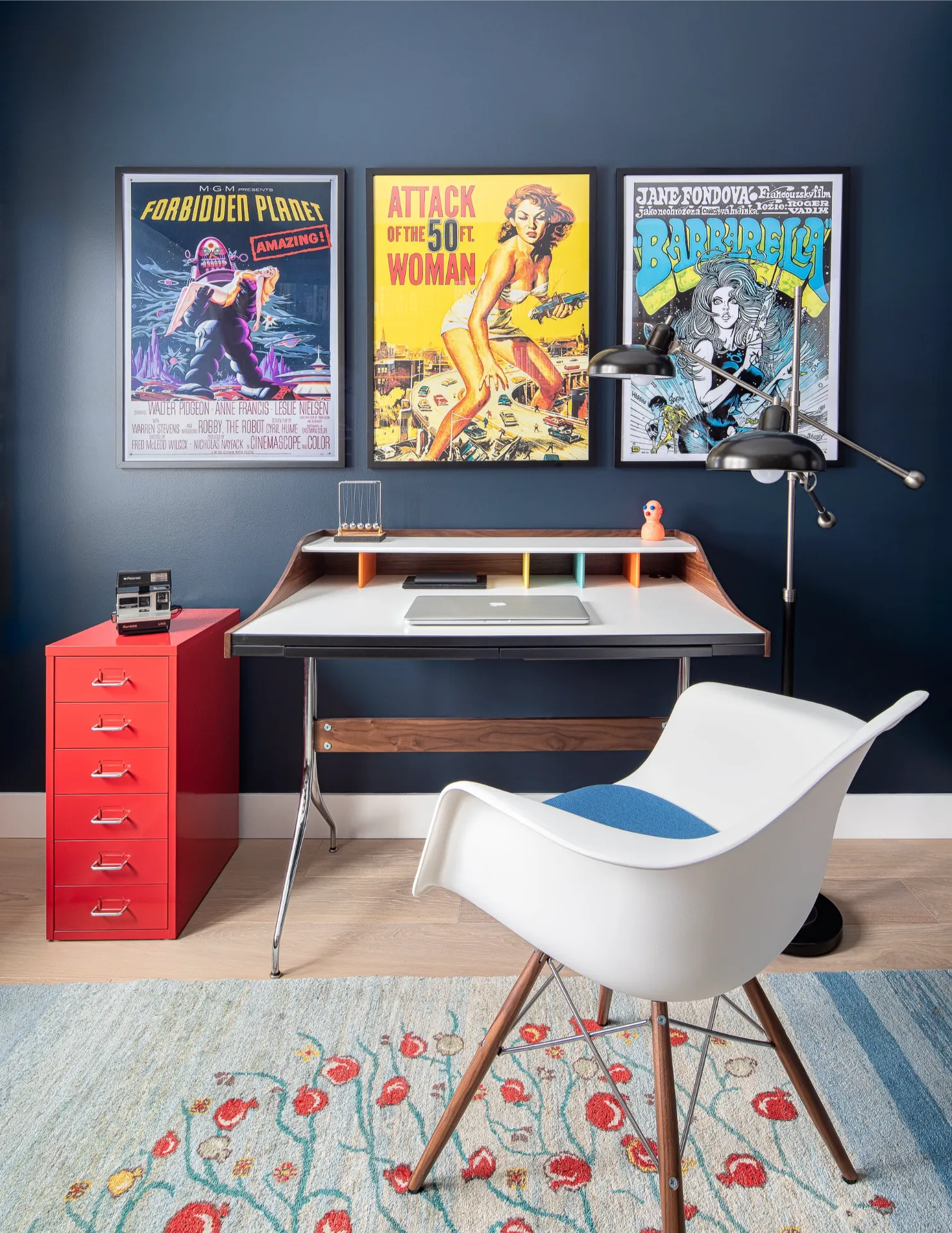 Home office with dark blue walls, vintage sci-fi movie posters, and a mid-century desk