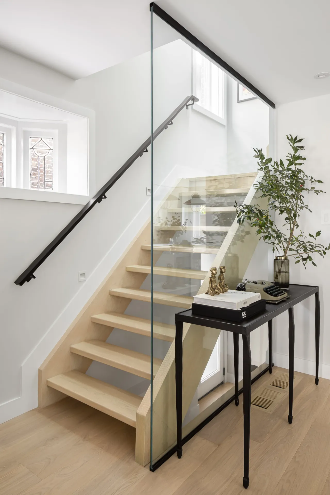 Modern light oak staircase with a black wall handrail and frameless glass guard