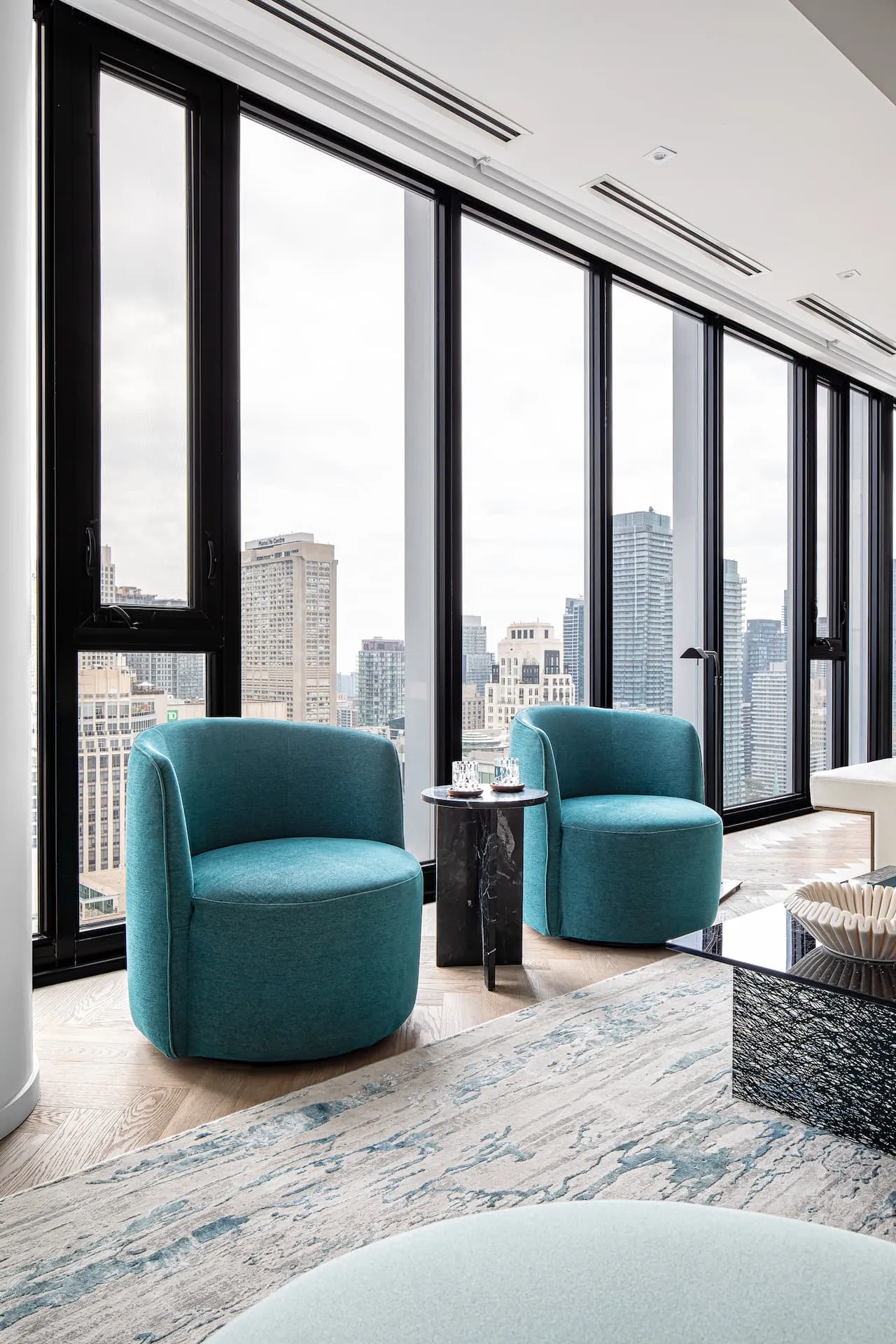Pair of aqua blue Italian swivel armchairs positioned by floor-to-ceiling windows overlooking the Toronto skyline.