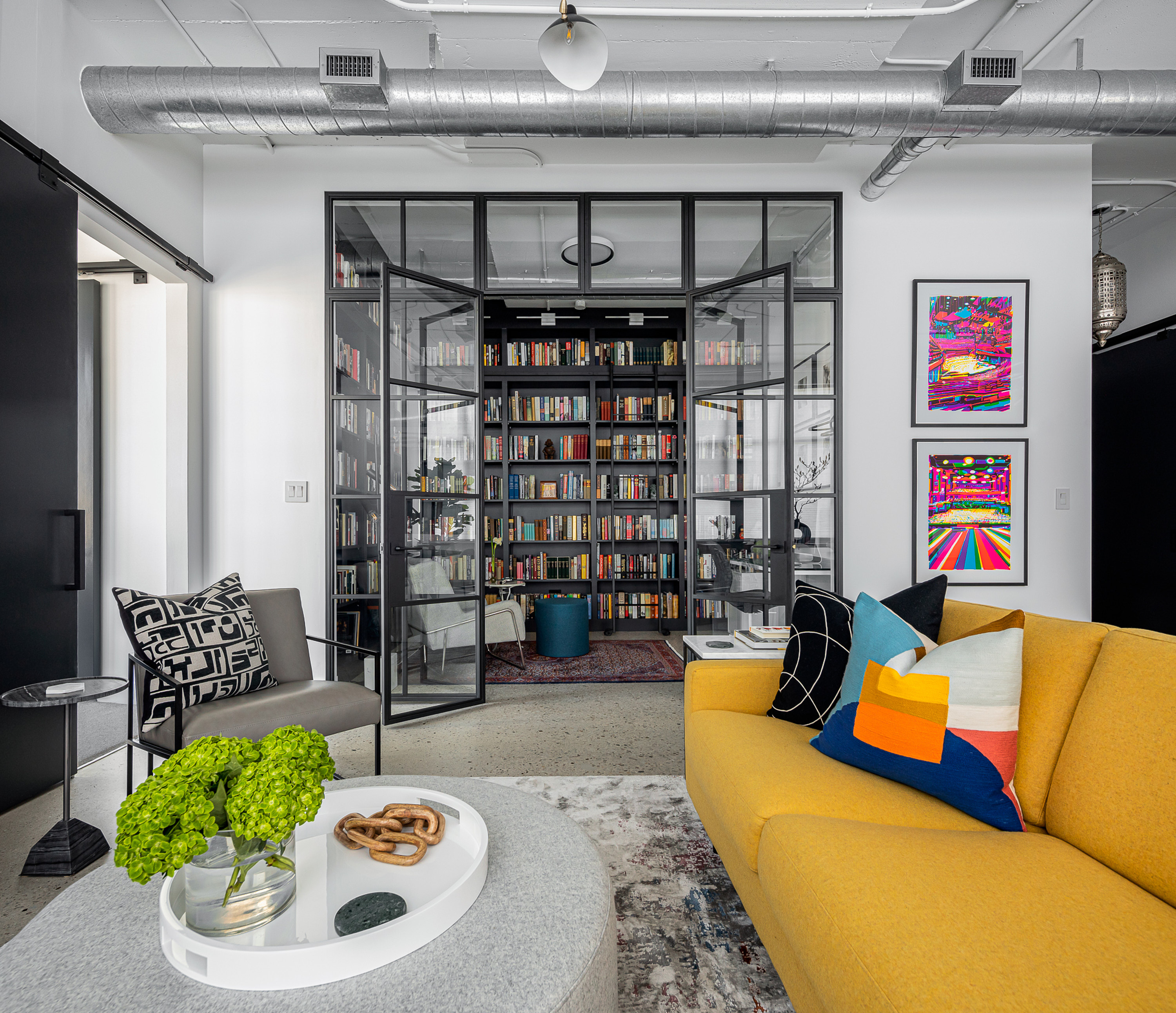 Eglinton loft Toronto industrial living room with large yellow sectional sofa, custom 10-foot steel-framed glass library doors. Creating a beautiful home library design.