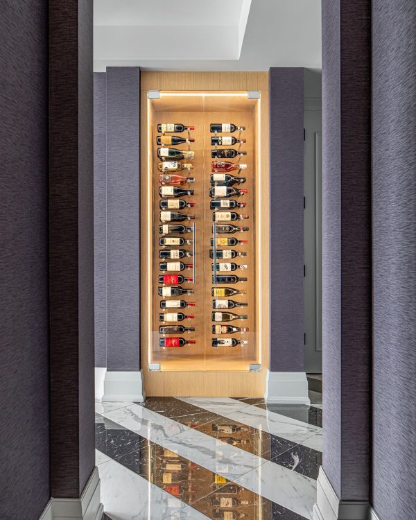 Angled view of a lit wine display with frameless glass door, oak veneer interior, and colourful artwork on dark wallcovering