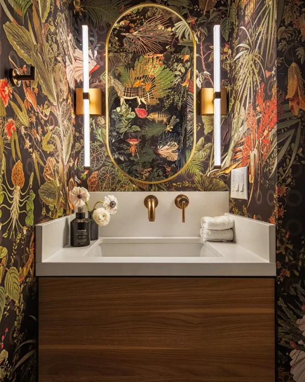 Walnut floating vanity with brass fixtures and oval mirror against dark botanical wallpaper