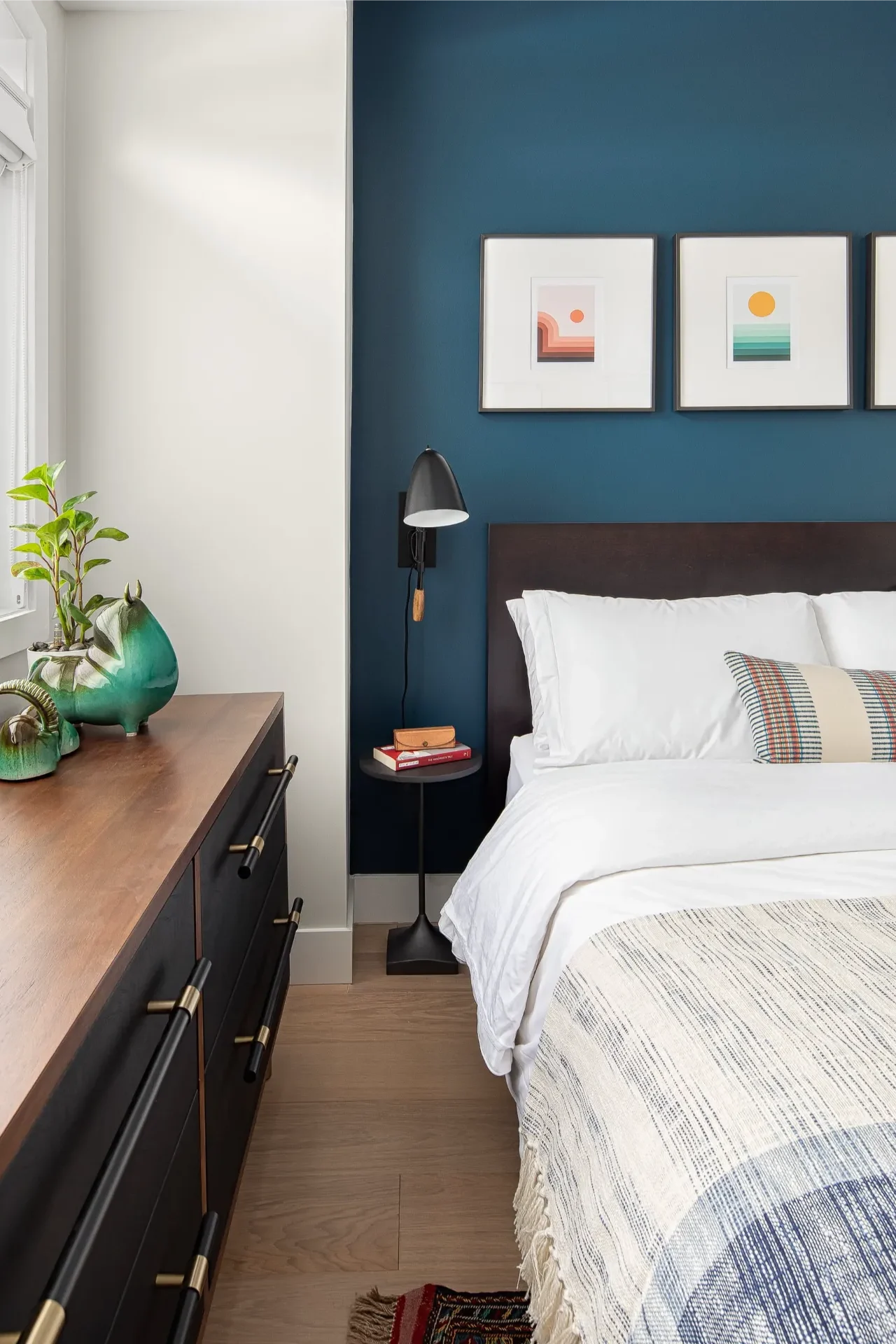 Bed with white linens against a dark blue wall with three framed landscape prints