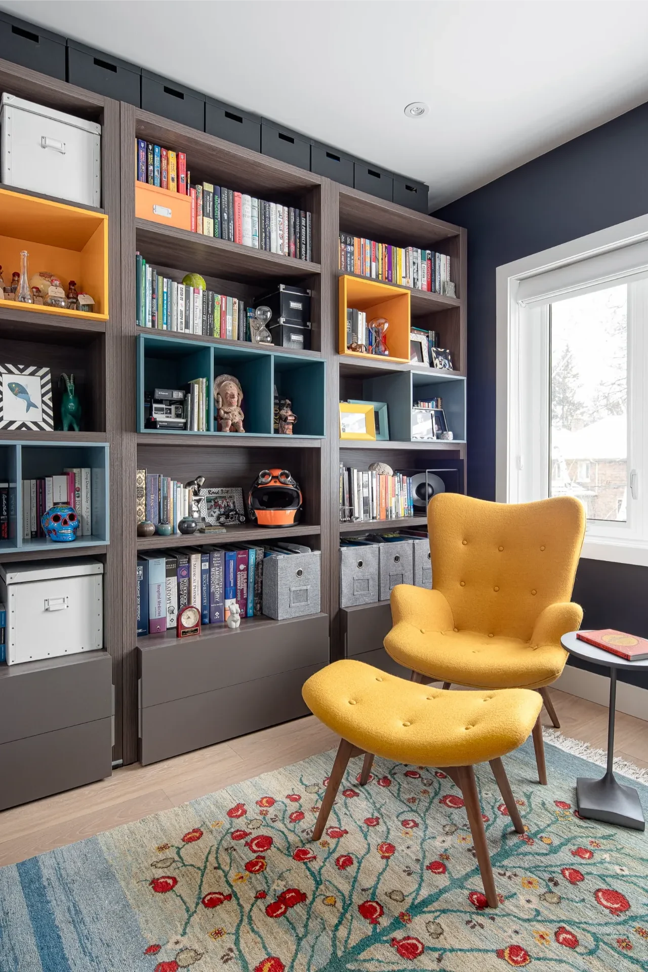 Dark wood built-in bookcases with teal and yellow cubbies and a yellow armchair