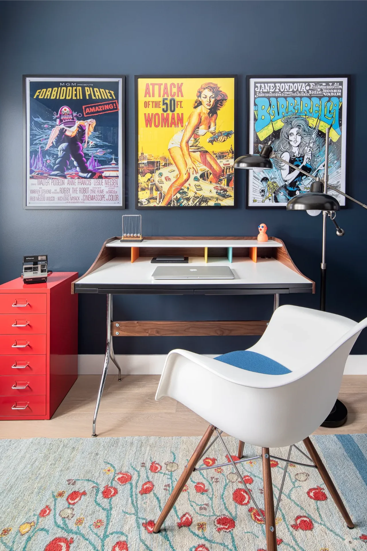 Home office with dark blue walls, vintage sci-fi movie posters, and a mid-century desk