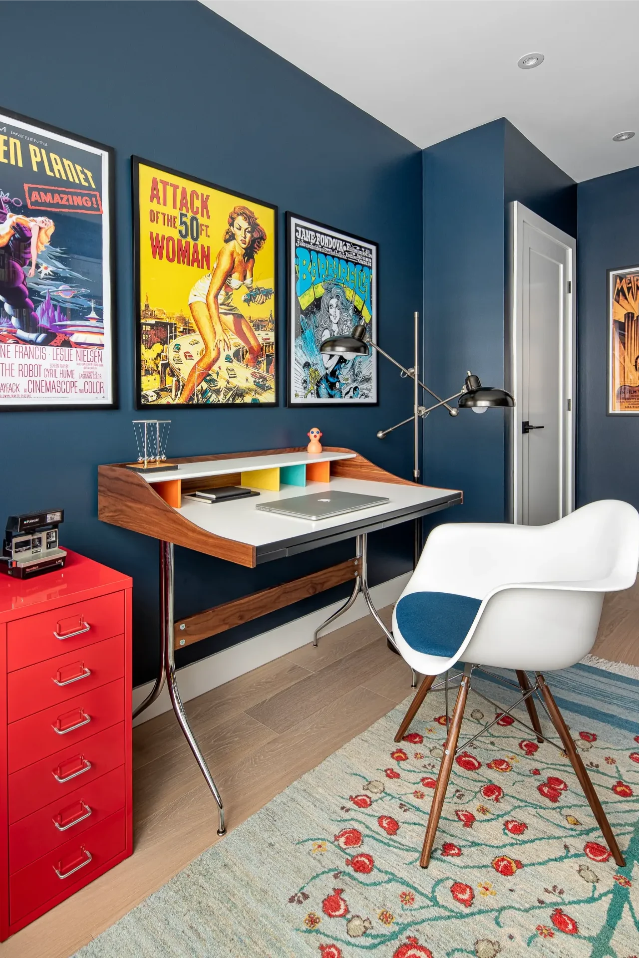 White modern chair at a mid-century desk with a red filing cabinet and vintage movie posters